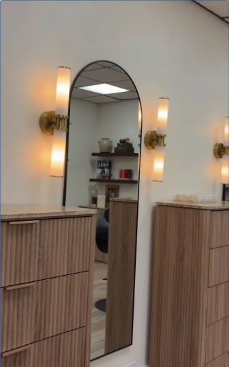 Arched styling mirror between warm wall sconces and wood cabinets